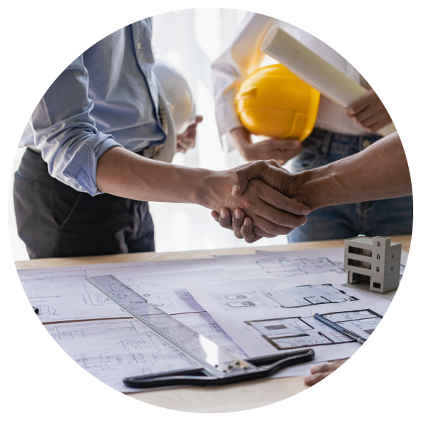 Three men holding hard hats are conversing over a desk with architectural plans and a model of a building; two of the men are shaking hands.